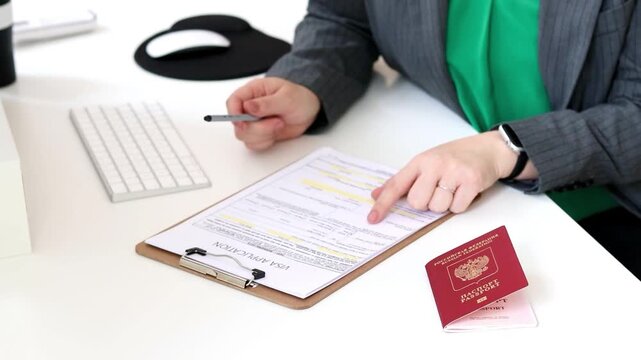 Close up of a caucasian woman filling out visa application documents with a Russian passport on a office table