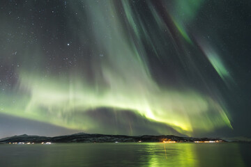 Explosion of corona colorful show of the Aurora Borealis, glowing in shades of pink, green, above fjord in northern Norway