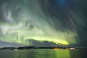 Explosion of corona colorful show of the Aurora Borealis, glowing in shades of pink, green, above fjord in northern Norway