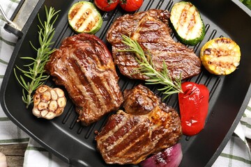 Pan with grilled beef steaks, rosemary and vegetables on table, top view