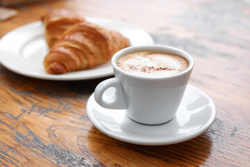 Aromatic coffee and tasty croissant on wooden table, closeup