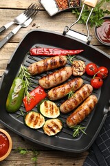 Pan with grilled sausages, vegetables, spices and sauces on wooden table, flat lay