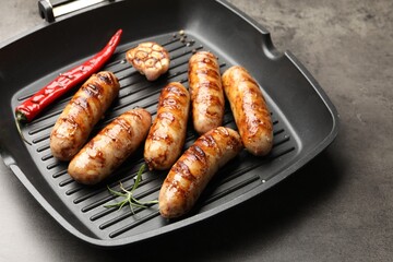 Pan with grilled sausages and spices on gray textured table, closeup