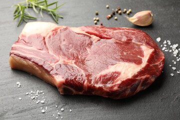 Piece of raw beef meat and spices on black table, closeup