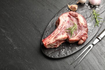Piece of raw beef meat, spices and carving fork on black table, above view. Space for text