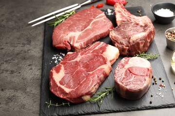 Pieces of raw beef meat, spices and carving fork on grey table, closeup