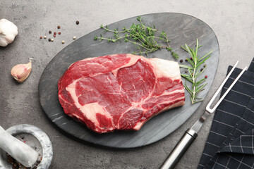 Piece of raw beef meat, spices and carving fork on grey table, flat lay