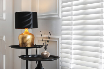 Stylish lamp and reed air freshener on black tables near white wall indoors. Space for text
