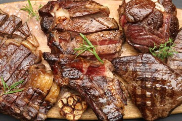 Pieces of tasty grilled beef with rosemary on wooden board, flat lay