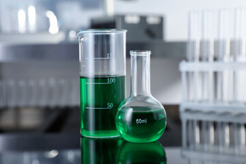 Glass beaker and flask with green liquid on table in laboratory, closeup
