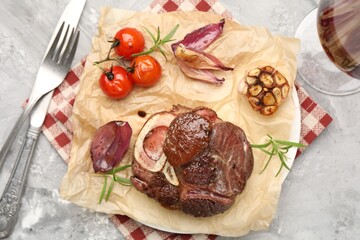 Tasty cut beef steak served with rosemary, garlic, tomatoes and wine on grey textured table, flat lay