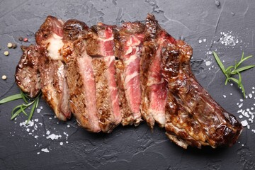 Tasty cut beef steak, salt, peppercorns and rosemary on black table, flat lay