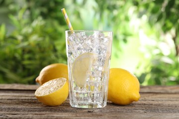 Refreshing water with lemon, ice and fruits on wooden table against blurred background