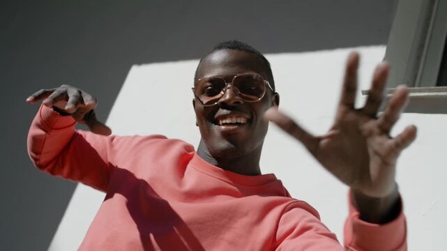 Happy young man wearing pink sweatshirt and aviator sunglasses dancing looking at camera low angle video portrait