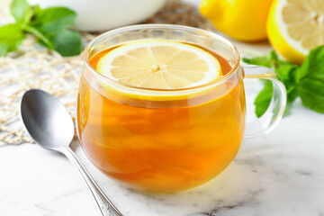 Aromatic tea in cup with lemon, mint and spoon on white marble table, closeup