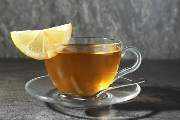 Aromatic tea in cup with lemon and spoon on grey table, closeup