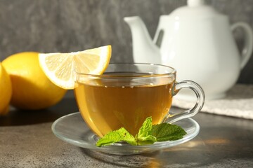 Aromatic tea in cup with lemons and mint on grey table, closeup