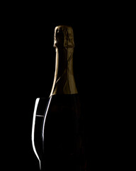 Artistic low-key still life of a champagne or sparkling wine bottle wrapped in golden foil, photographed against a dark black background with dramatic side lighting