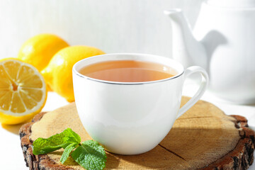 Aromatic tea in cup, lemons, mint and teapot on table, closeup