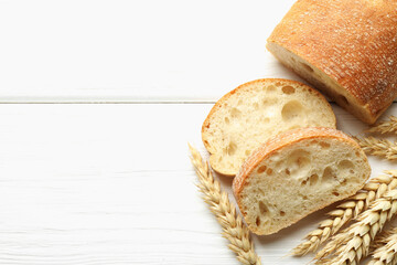 Cut crispy ciabatta and wheat ears on white wooden table, flat lay. Space for text
