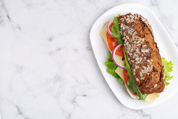 Tasty ciabatta sandwich with cheese and vegetables on white marble table, top view. Space for text