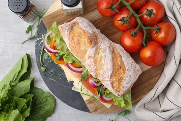 Delicious ciabatta sandwich with prosciutto, cheese and vegetables on light grey table, flat lay