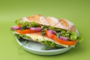 Delicious ciabatta sandwich with prosciutto, cheese and vegetables on green background, closeup