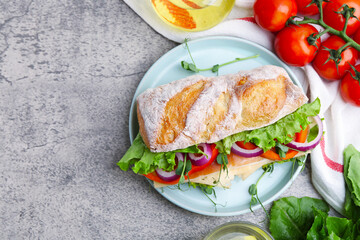 Delicious ciabatta sandwich with prosciutto, cheese and vegetables served on light grey table, flat lay. Space for text