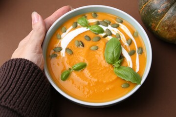 Woman with delicious pumpkin soup on brown background, above view
