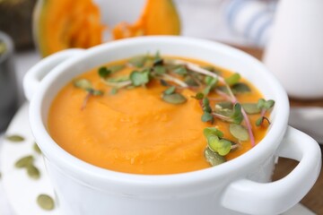 Delicious pumpkin soup with seeds and microgreens in bowl on table, closeup