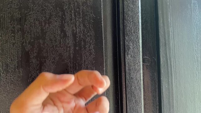 Close-up shot of a human hand knocking or rapping knuckles against a dark, textured black wooden door, symbolizing visit, waiting, or entry.