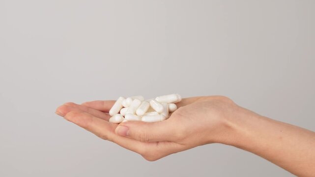 Hand holding a pile of white capsules on a neutral background with copy space. Concept of dietary supplements, vitamins and healthcare pills.