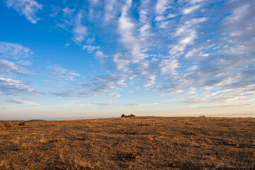 A vast, arid landscape stretches beneath a blue sky streaked with scattered clouds