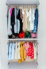 Open wardrobe with various clothes neatly hanging on wooden hangers, organized clothing storage