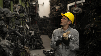 A factory worker wearing a safety helmet inspecting used car parts