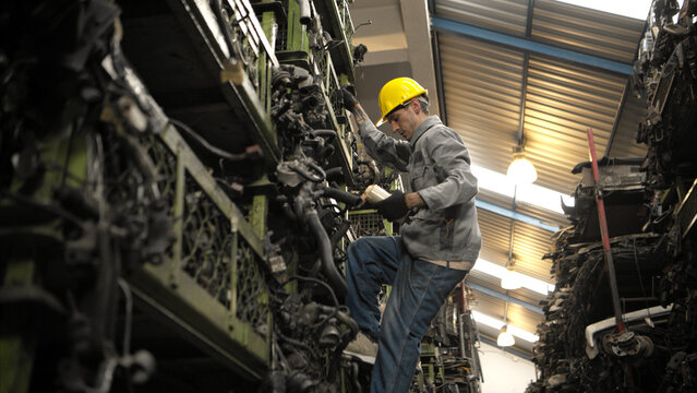 A factory worker wearing a safety helmet inspecting used car parts