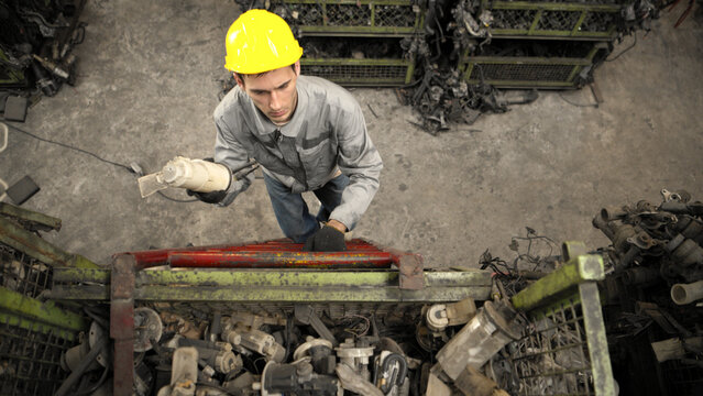 A factory worker wearing a safety helmet inspecting used car parts