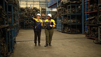 Two female engineers wearing safety gear inspecting car parts inventory