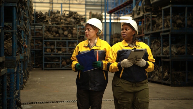 Two female engineers wearing safety gear inspecting car parts inventory