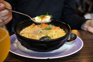 A woman eats ramen, Japanese miso ramen noodles with fried pork and egg, drizzled with sauce.