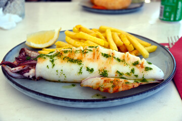 Grilled whole squid with fries, served with lemon, on a plate. Seafood concept, calamari