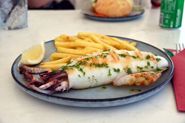 Grilled whole squid with fries, served with lemon, on a plate. Seafood concept, calamari