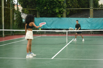 African woman prepares to serve against Asian opponent during a mixed tennis match, symbolizing diversity and competition