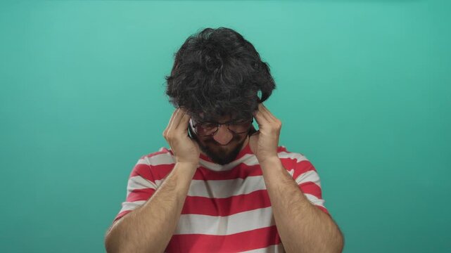 Young man with beard in striped shirt looking stressed against green background.