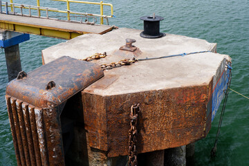 concrete mooring dolphin with rusty chains and fender at a marine dock, used for securing ships and boats, showing weathered metal surface and industrial maritime details