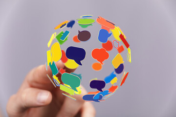 Hand holding global sphere made of colorful speech bubbles, representing communication, social...