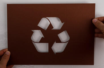 Recycling symbol cut from brown paper held by hands, illustrating environmental consciousness and...