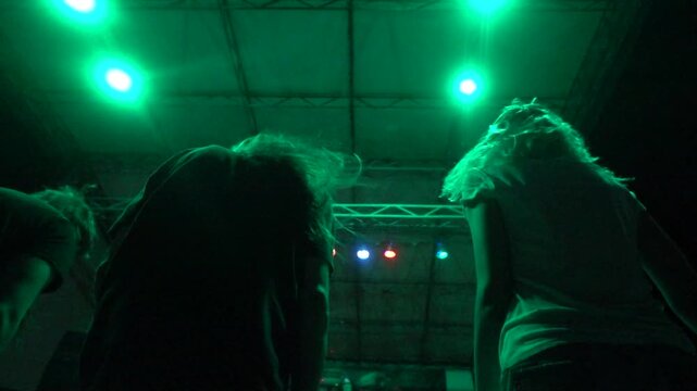 Energetic concertgoers headbanging, shaking their hair under vibrant stage lights at a lively motorbike festival, captured in dynamic motion from a low angle.