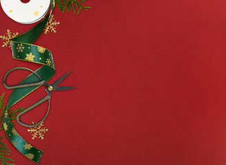 Paper spool of green Christmas ribbon with golden snowflakes, scissors and green evergreen twigs for holiday gift wrapping on red background