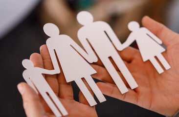 Close-up shot of a hand holding a paper cutout of a family, symbolizing family values, love, and...